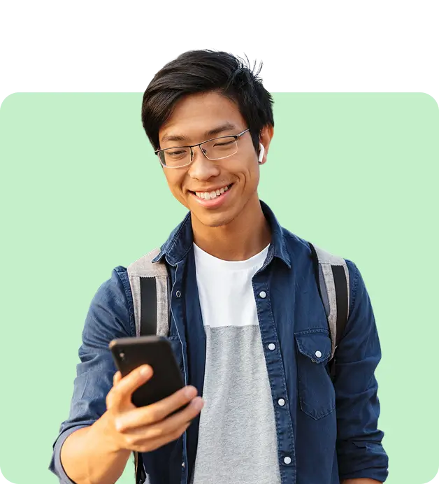 Smiling male undergraduate student looking at his smartphone while holding a backpack